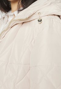 Gevoerde jas in lichtroze met een quilted ontwerp, voorzien van een capuchon, gouden ritssluiting en een trekkoordverstelling bij de kraag.