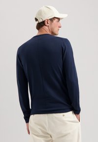 Marineblaue Langarmshirt mit Rundhalsausschnitt, schlanker Passform und glatter Textur, kombiniert mit einer hellen Baseballkappe im Cordura-Muster.