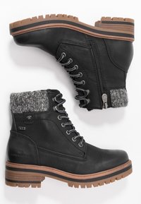 Bottes en cuir noir pour cheville avec semelles à crampons marron, poignets en tricot gris, devant à lacets et fermetures éclair latérales, vues de côté et de la semelle.