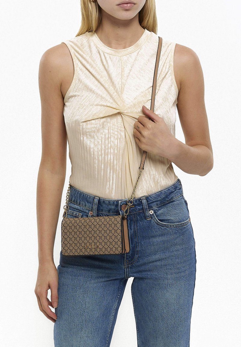 Borsa a tracolla marrone con motivo esagonale e un dettaglio in pelle, dotata di una tracolla a catena. Indossata con un top crema e jeans blu.