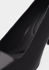Μαύρο δερμάτινο παπούτσι με ψηλό τακούνι και στρογγυλεμένη μύτη, με λείο φινίρισμα, φαίνεται από κεκλιμένη πάνω όψη με έμφαση στο πάνω μέρος και την εσωτερική επένδυση.