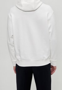 Felpa bianca con cappuccio, caratterizzata da una morbida texture e un design casual. I polsini e l'orlo a coste completano l'aspetto, abbinati a pantaloni scuri.