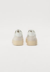 White sneakers featuring a suede and leather upper, rounded silhouette, and textured sole in a light beige color.