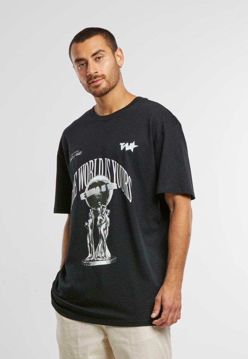 T-shirt oversize unisexe noir en coton. Présente une impression graphique blanche d'un globe et de figures avec le texte "LE MONDE EST À VOUS".