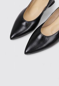 Zapatos de cuero negro con punta afilada y tacón bajo. La superficie es lisa con un acabado brillante, y cuenta con un ligero corte en la parte superior.