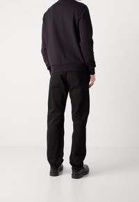 Felpa nera con colletto rotondo, abbinata a jeans neri. I jeans presentano tasche posteriori e sono indossati con scarpe nere.