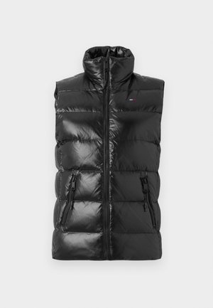 Melna pūkainā veste ar augstu apkakli, spīdīgu apdari, priekšējo rāvējslēdzēju un divām sānu kabatām ar rāvējslēdzējiem; ar šūtiem, polsterētiem segmentiem.