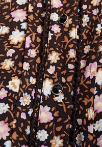 Blouse à imprimé floral foncé avec un fond noir orné de fleurs roses, bleues et crème, agrémentée de coutures décoratives et de boutons noirs.