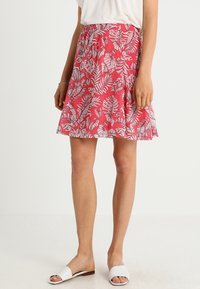 Gonna rossa con motivo floreale bianco a foglie, realizzata in tessuto leggero. Il design presenta una vita elastica e una silhouette svasata.