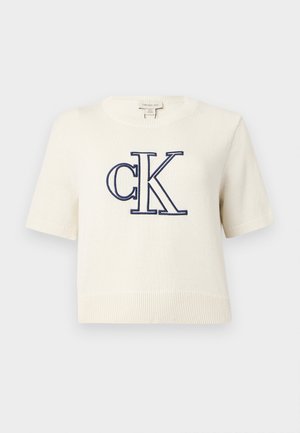 Pulover alb cu mâneci scurte tricotat, cu tiv și manșete cu dungi, având logo-ul mare „cK” bleumarin brodat pe față.