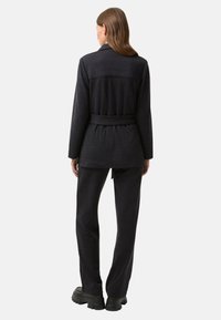 Ensemble en tricot gris charbon comprenant un long blazer à taille ceinturée et un pantalon à jambes larges. Texture douce et coupe décontractée tout au long.