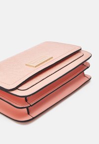 Ljusrosa plånbok i konstläder med strukturerad ytfinish, svart kant och en guldfärgad platta på framsidan. Tre synliga fack.