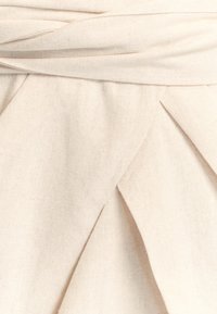 Krémová látka s textúrovanou väzbou, s prekladaním a skruteným detailom v páse, vytvárajúca vrstvený vzhľad.