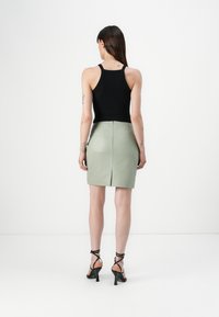 Svart ribbestrikket tanktopp, høyhudet grønn blyantskjørt med splitt bak, og svarte sandaletter med stropper og høy hæl. Enkle tilbehør, minimalistisk design.