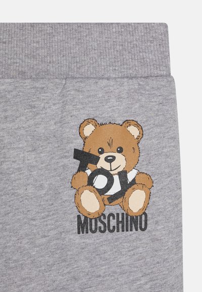Pantalones de chándal de algodón gris con un gráfico de un oso de dibujos animados sosteniendo un juguete en blanco y negro. El texto "Moschino" está impreso debajo del oso.