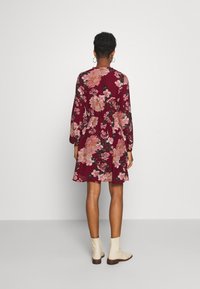 Vestido floral burdeos con mangas largas y cintura ajustada, con patrones de flores rosas y verdes. Combinado con botas de tobillo color crema.