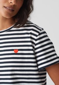 Gestreept T-shirt met marineblauwe en witte horizontale strepen, met een kleine rode hartborduursel op de linkerborst. Korte mouwen.