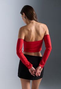 Red off-the-shoulder crop top with long sleeves, paired with a fitted black mini skirt, showcases smooth textures and a form-fitting design.