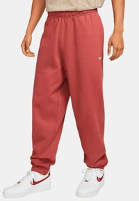 Pantalones de chándal rojos con cintura elástica y bolsillos laterales, hechos de material suave, que presentan un pequeño logo blanco de Nike en el muslo izquierdo.