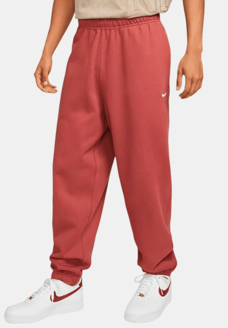 Pantalones de chándal rojos con cintura elástica y bolsillos laterales, hechos de material suave, que presentan un pequeño logo blanco de Nike en el muslo izquierdo.