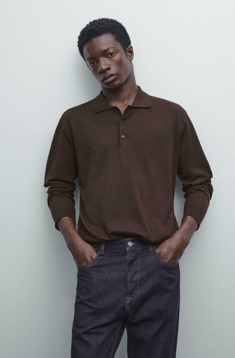 Donkerbruin poloshirt met lange mouwen, een kraag en drie knopen, gecombineerd met donkere spijkerbroeken. De stof lijkt zacht met een gladde textuur.