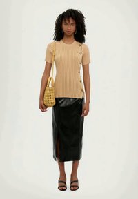 Beige ribbestrikket topp med korte ermer og knappedetaljer, parret med et svarte lær midi-skirt med sideslitt. Vevd gul håndveske.