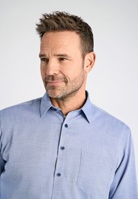 Lichtblauwe button-up blouse met een subtiel textuurpatroon, lange mouwen en een borstzak. Voorzien van donkerblauwe knopen en een klassieke kraag.