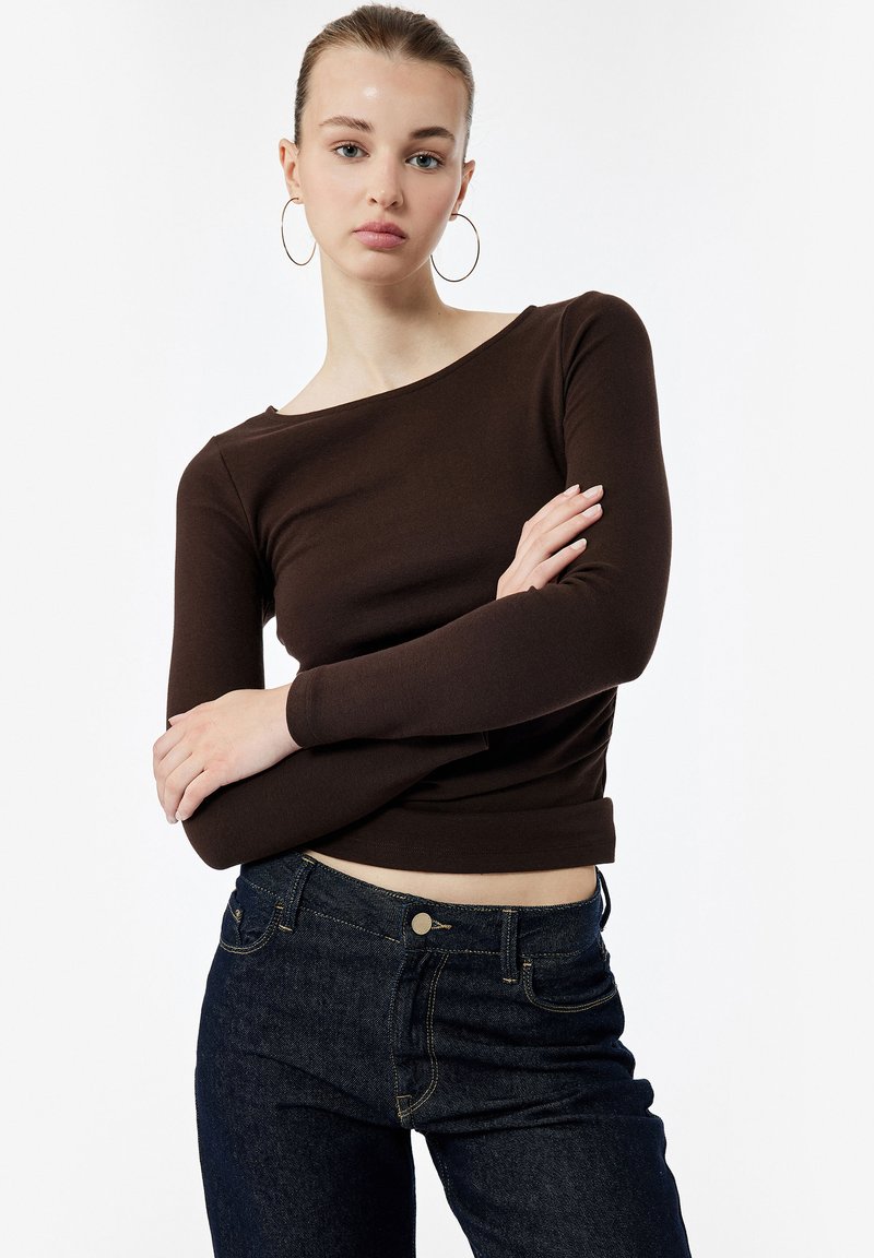 Brun langærmet top i en tætsiddende design med rund halsudskæring, parret med mørk denim jeans med en klassisk pasform og gyldne syninger.