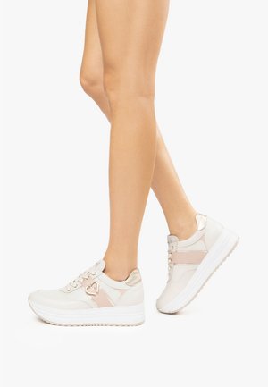 Baskets blanches et beiges avec un accent métallique, dotées d'une semelle surélevée, d'un design à lacets et d'un détail en forme de cœur sur le côté.