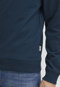 Navyblauwe sweatshirt met ribbelboorden en -zoom, voorzien van een klein label aan de zijkant. Glad textuur, casual pasvorm.