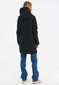 Veste à capuche noire au design élégant, silhouette longue et capuche réglable. Associée à un jean en denim bleu et des chaussures de couleur claire.