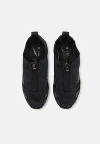 Juodi slip-on batai su tekstūruotu paviršiumi, turintys centrinį užtrauktuką ir guminius akcentus, apvaliu pirštu ir taškiniais raštais šonuose.
