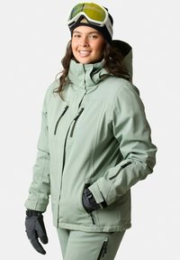 Light green insulated ski jacket with multiple zippers, high collar, and attached hood. Paired with black gloves.
