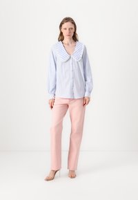 Camicia a righe in azzurro chiaro e bianco con un ampio colletto rifinito in pizzo, abbinata a pantaloni dritti rosa chiaro e tacchi trasparenti.