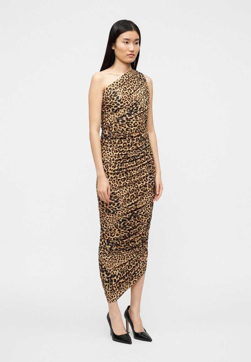 Robe asymétrique à imprimé léopard avec texture froncée, ourlet au genou et coupe ajustée. Le modèle porte des escarpins noirs.