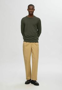 Olivgrön långärmad tröja i avslappnad passform ihop med beige byxor. Outfitten kompletteras med svarta skor.