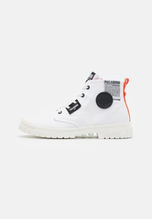 Witte hoge sneakers met een gestructureerde rubberen zool, zwart logo patch, oranje accent en zwarte veters op een gladde stoffen bovenkant.