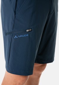 Pantalones cortos azul marino hechos de tejido ligero, con un bolsillo con cremallera y un logo visible en el lado izquierdo.