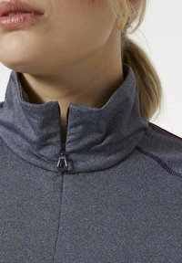 Giacca grigia con colletto alto e zip, realizzata in un tessuto texturizzato con una finitura liscia. Dettaglio con zip sul collo e cuciture a contrasto.
