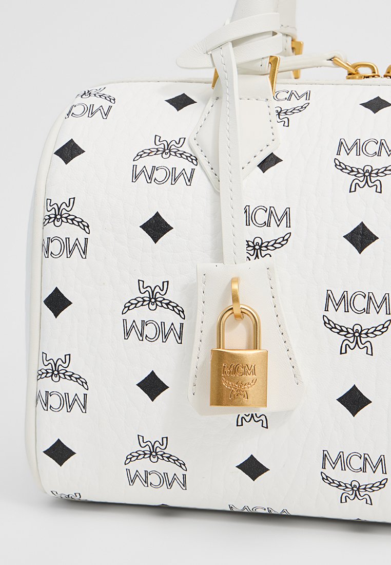 Weißes Lederhandtasche mit schwarzem MCM-Logo-Muster, Rautenformen und einem goldfarbenen Vorhängeschloss-Detail an der Seite.