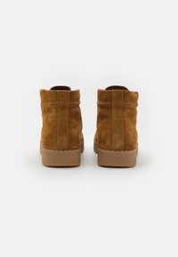 Botas de tobillo de ante color beige con punta redondeada, diseño minimalista, superficie texturizada y suela de goma de color beige claro.