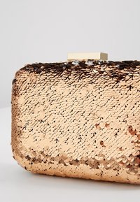 Gul paljetterad kuvertväska med rektangulär form, som har en sl�ät yta och ett platt guldspänne på toppen.