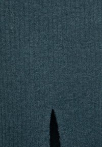 Dunkelblauer Strickstoff mit weicher Textur, der ein zentrales Schlitzdetail aufweist. Das Material wirkt warm und dicht mit einer dezenten gerippten Oberfläche.