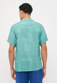 Camisa de mangas curtas em azul claro com padrão de bandana. Apresenta um corte relaxado, gola plana e uma textura suave e macia.