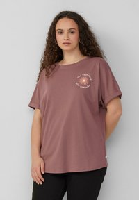 Roze katoen T-shirt met opgerolde mouwen, voorzien van een bloemenafbeelding en de tekst "VUL JE DAGEN MET ZONNESCHIJN" in pastelkleuren.
