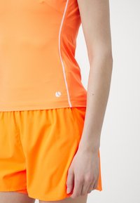 Oranssi urheilullinen tankkitoppi valkoisilla yksityiskohdilla ja siihen sopivat oranssit shortsit. Kankaan näyttää olevan sileä, kevyt ja sopii aktiiviseen pukeutumiseen.