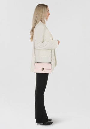 Pink crossbody bag with a silver chain strap and a metal clasp, carried by a person in a white blazer and black flared pants.