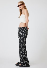 Svarta byxor med blommönster och avslappnad passform, ihop med en vit ribbad kort topp. Outfiten har midja med dragsko och platta sandaler.