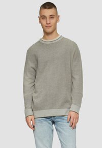 Szary sweter z dzianiny o teksturowym splocie, okrągłym dekolcie oraz kontrastowymi ściągaczami na mankietach i u dołu. Nosi się go na jasnoniebieskich dżinsach.