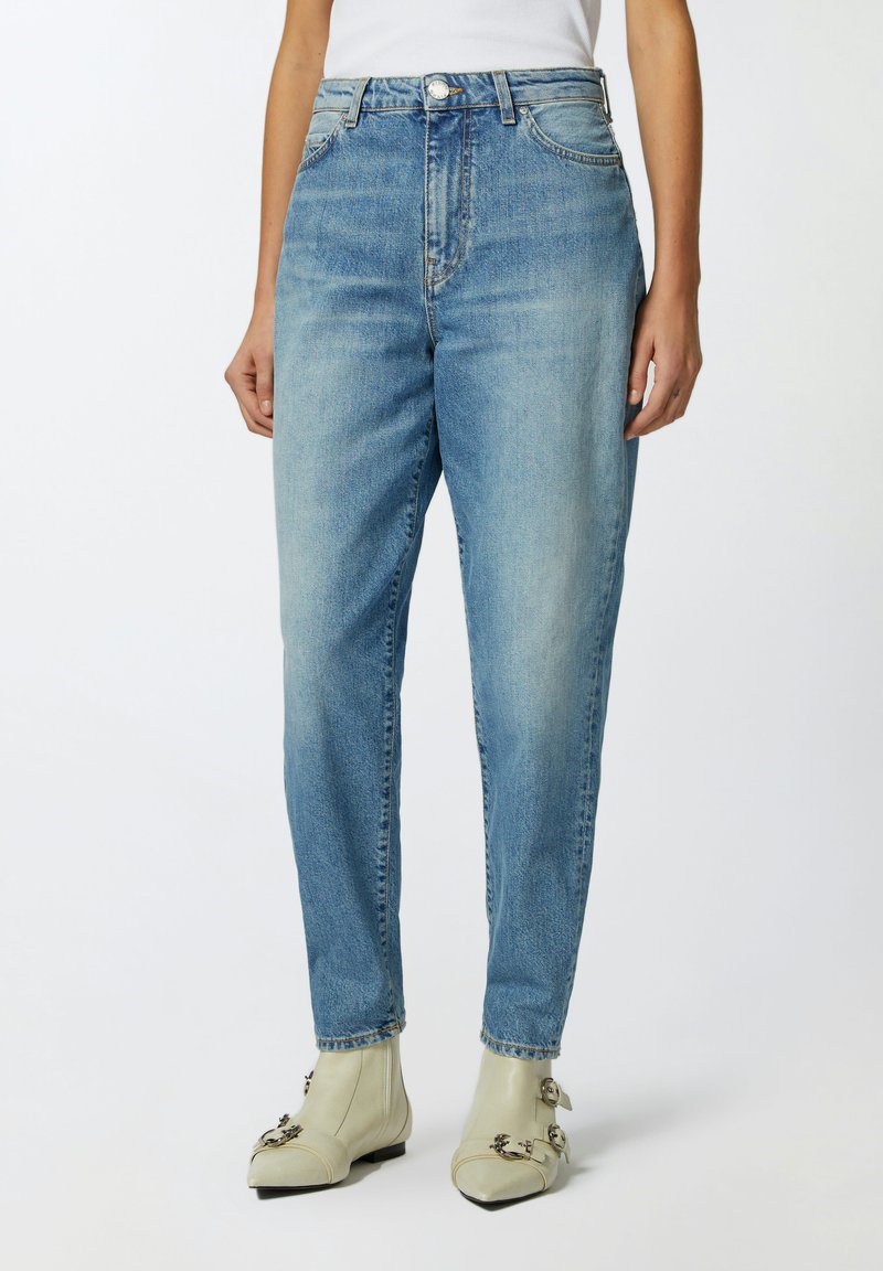 Jeans azzurri chiari a vita alta con taglio dritto, lavaggio sbiadito, design a cinque tasche e chiusura con bottone metallico, abbinati a stivali grigi chiari.